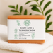 Kojic Acid & Turmeric Soap bar with RK label on a white towel with green leaves in the background